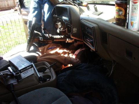 1990 Ford Bronco - A person is working on the interior of a vehicle, with tools and parts scattered around the dashboard and console area.