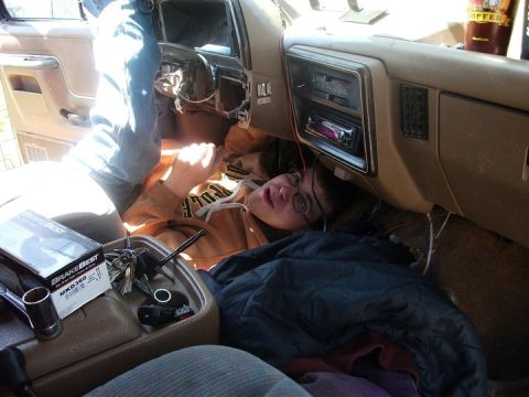 1990 Ford Bronco - A person works on the dashboard wiring of a 1987 Ford F-150, with tools and parts visible in the cabin.
