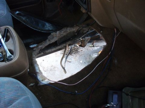 1990 Ford Bronco - The interior floor of a vehicle shows significant damage and exposed wiring, with tools lying nearby.