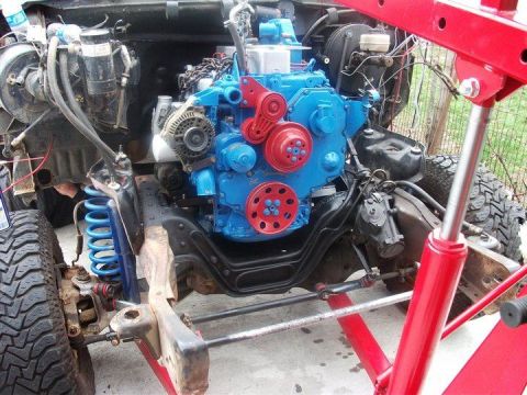 1990 Ford Bronco - A bright blue and red engine is being lowered into a vehicle's chassis with the help of an engine hoist.
