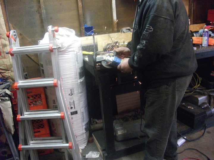 Person using an angle grinder in a workshop with a ladder and large bag