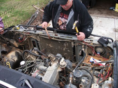 1990 Ford Bronco - A man works on the engine bay of a vehicle, with tools in hand. The engine block has some visible text.