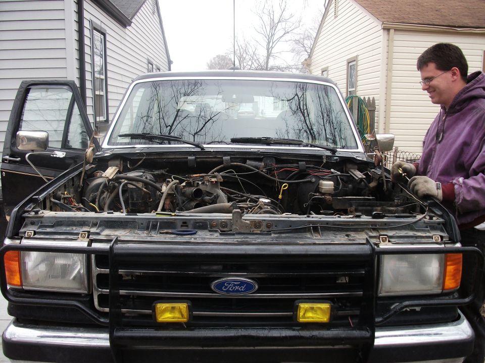 Black Ford Bronco with hood open, showing engine compartment and a man working on it