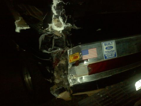 1990 Ford Bronco - The rear of a vehicle shows significant damage, with stickers including an American flag and 'Built Ford Tough'.