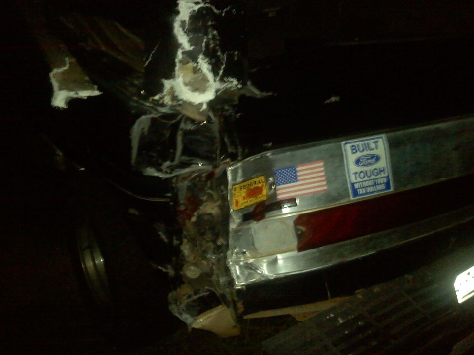 Rear of a damaged vehicle with an American flag sticker and a 'Built Ford Tough' sticker