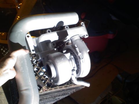 1990 Ford Bronco - A turbocharger assembly with intake piping is shown, held by a hand and placed on a metal grate.