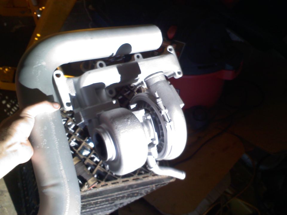 Turbocharger assembly with intake piping held by a hand, resting on a metal grate