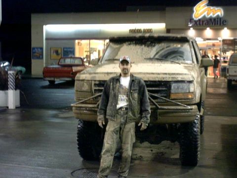 1995 Ford Bronco - A man poses with his heavily mud-caked pickup truck in front of a gas station at night.