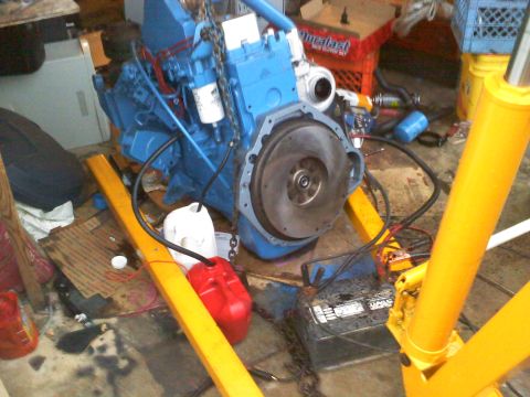 1990 Ford Bronco - A blue engine, possibly a 4BTA swap, is mounted on an engine stand with a turbocharger visible. Red and white fuel cans are on the floor.