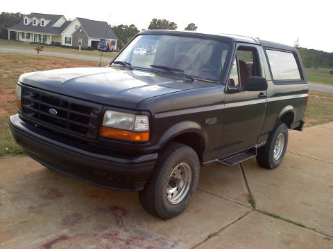 1995 Ford Bronco - This black Ford Bronco is parked on a concrete driveway in front of a house.
