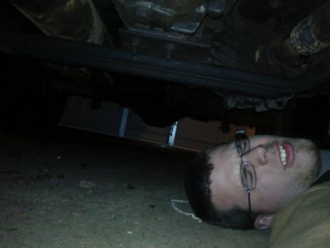 1995 Ford Bronco - A man lies on the ground looking up at the underside of a vehicle, with the Supermotors.net logo visible.