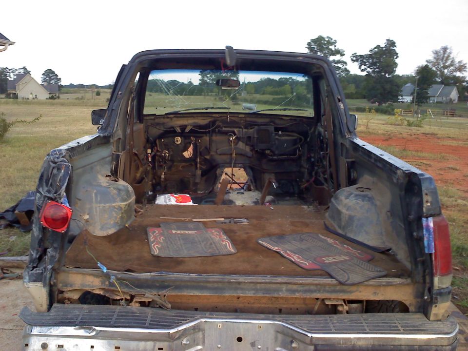 Rear view of a damaged 1992 Ford Bronco with its interior stripped and windshield cracked