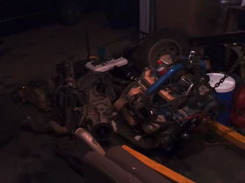 1995 Ford Bronco - Various engine and transmission parts are laid out on the ground, with a tire and storage containers visible.