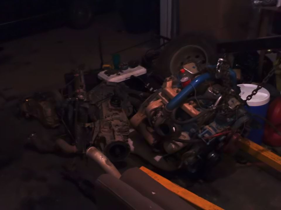 Engine and transmission components piled up, with a tire and some buckets nearby