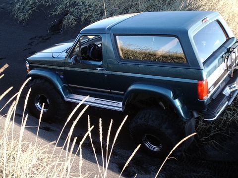 1996 Ford Bronco - This 1996 Ford Bronco is navigating a sandy landscape, with dry grass partially obscuring the view.