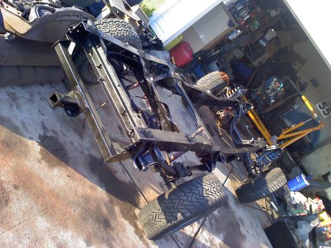 1995 Ford Bronco - The chassis and frame of a 1995 Ford Bronco, showing its suspension and tires, in a workshop setting.
