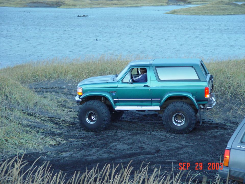 Teal lifted two-door Ford Bronco on big tires, side view by water
