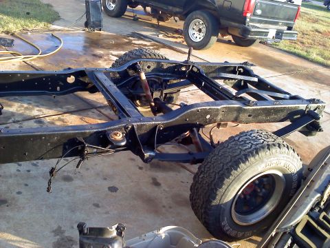 1995 Ford Bronco - The chassis of a vehicle is shown, with a black pickup truck in the background.