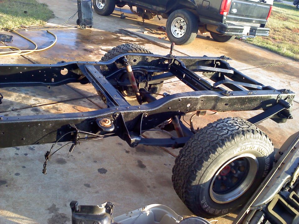 vehicle frame with suspension components and tires, black pickup truck in background