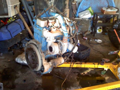 1995 Ford Bronco - Engine assembly with turbocharger and transmission bell housing is supported by a yellow engine stand.