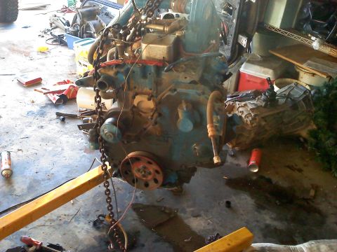 1995 Ford Bronco - An engine is suspended by chains from an engine hoist in a garage setting.