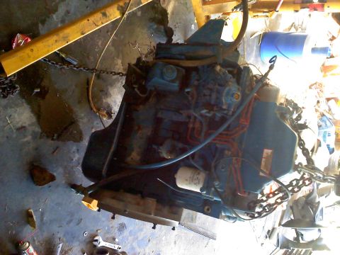 1995 Ford Bronco - Engine assembly being worked on, suspended by an engine hoist.