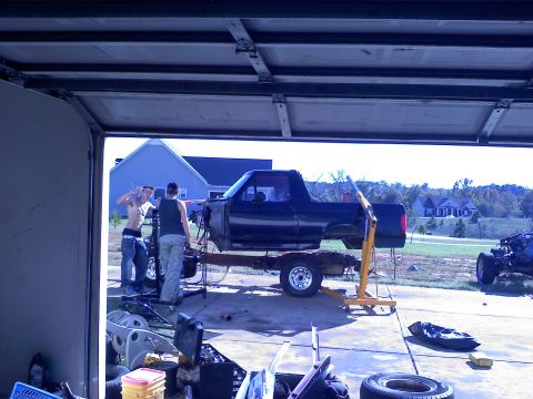 1995 Ford Bronco - A black Ford Bronco body is elevated on a trailer in a garage, with two individuals attending to it.