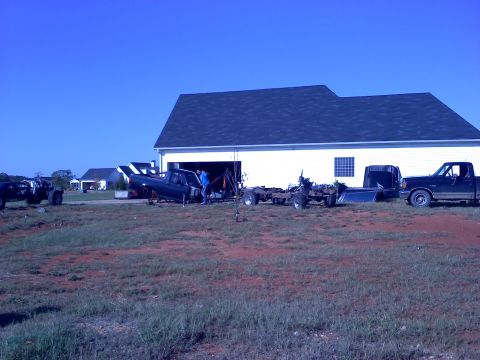 1995 Ford Bronco - Multiple trucks and parts are visible in a yard next to a garage, with a pickup truck parked nearby.