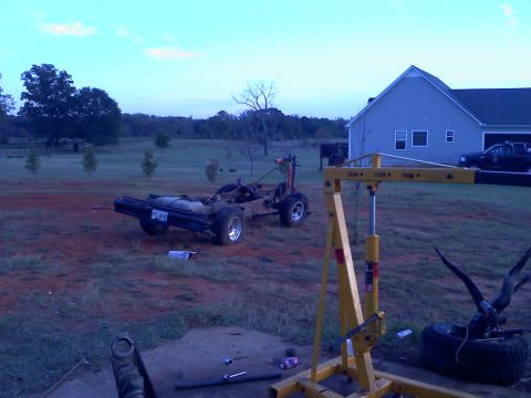 1995 Ford Bronco - Vehicle frame and engine hoist in a yard during the day.