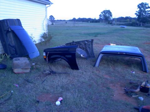 1995 Ford Bronco - Various disassembled parts of a Ford Bronco are scattered on the grass next to a house.