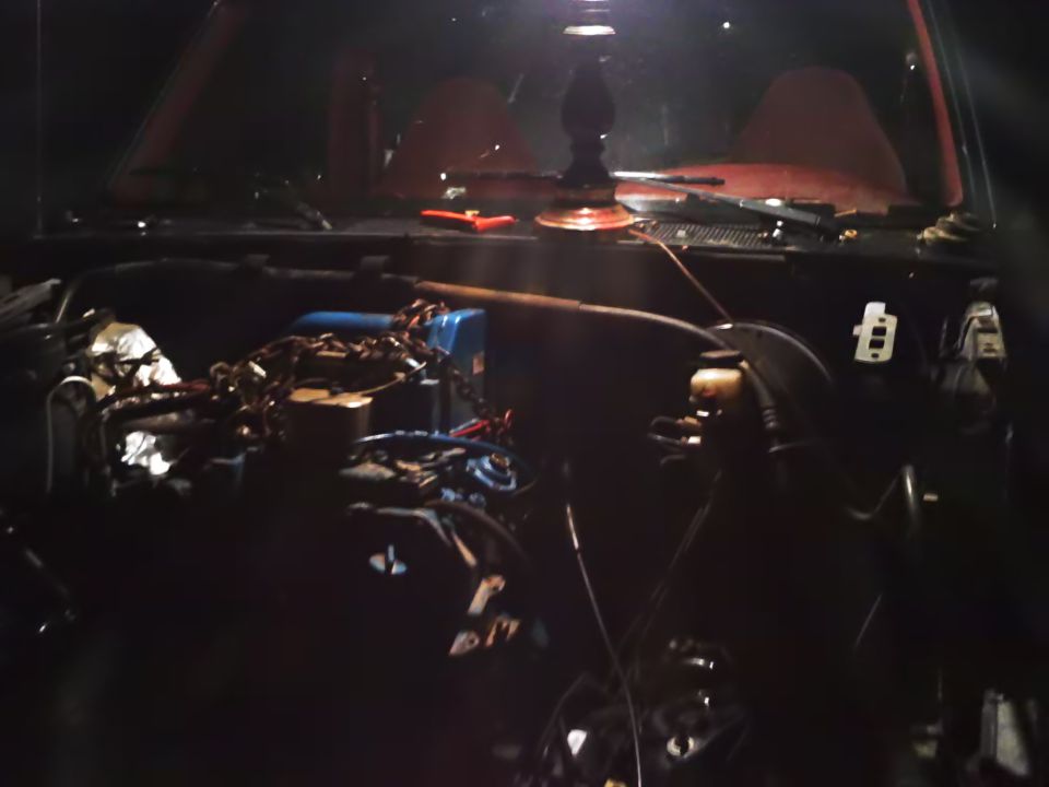 Engine bay with visible engine components, chains, and tools. Dark lighting