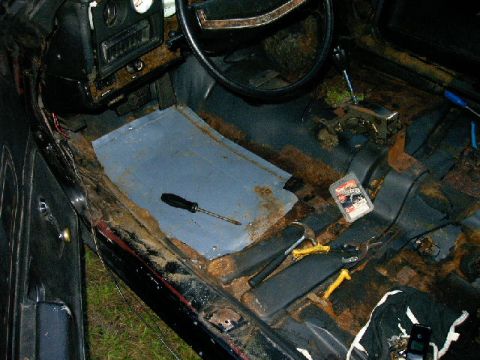 1975 Chevrolet Chevelle - The interior of a car shows significant rust and disarray, with tools scattered on the floor.