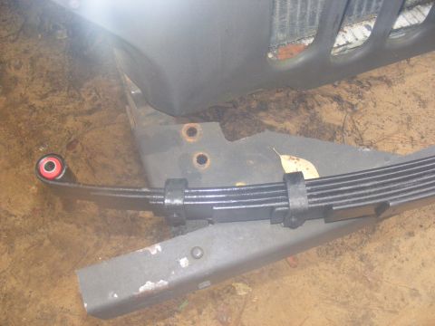 1978 Ford Bronco - A close-up view shows a leaf spring suspension component with a red and black bushing attached to the end. The spring is mounted to a black…