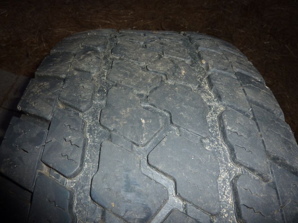 Close-up of a worn black tire tread with visible cracks and debris.