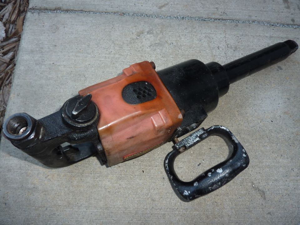 Orange and black pneumatic impact wrench with a black handle on concrete.