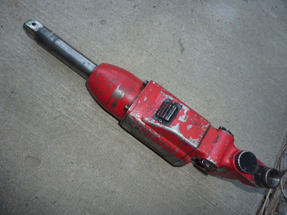 Red and silver pneumatic tool with square drive and threaded fitting on concrete.