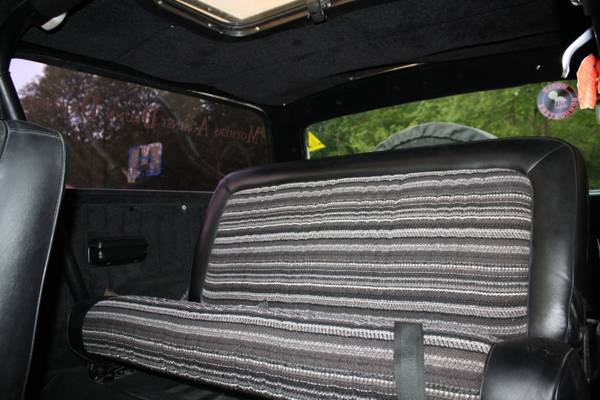 Interior rear bench seat of a vintage Ford Bronco with striped fabric and black vinyl.