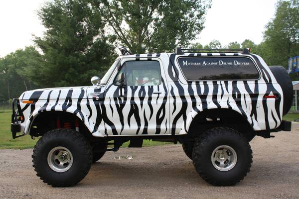 1979 Ford Bronco with zebra stripe paint, lifted, with "Mothers Against Drunk Drivers" on rear window.