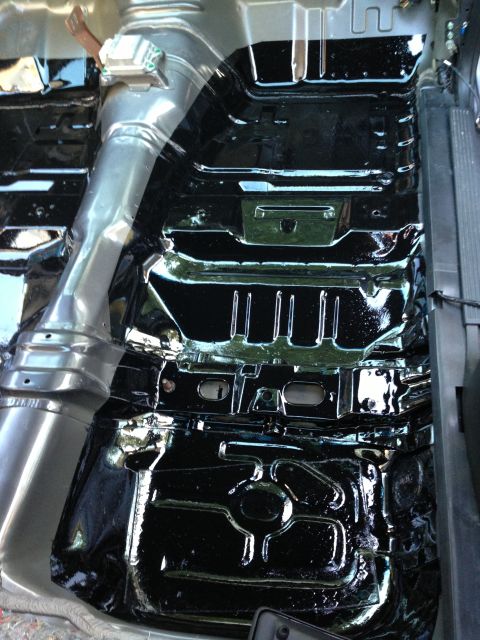 2004 Ford Crown Victoria - The interior floor of a vehicle has been coated in a glossy black protective material. A large metal exhaust pipe runs along the left side…