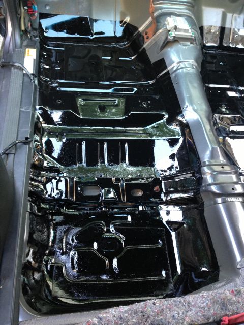 2004 Ford Crown Victoria - The black painted floor pan of a vehicle interior is shown, with visible structural reinforcements and wiring. A silver exhaust tunnel runs…