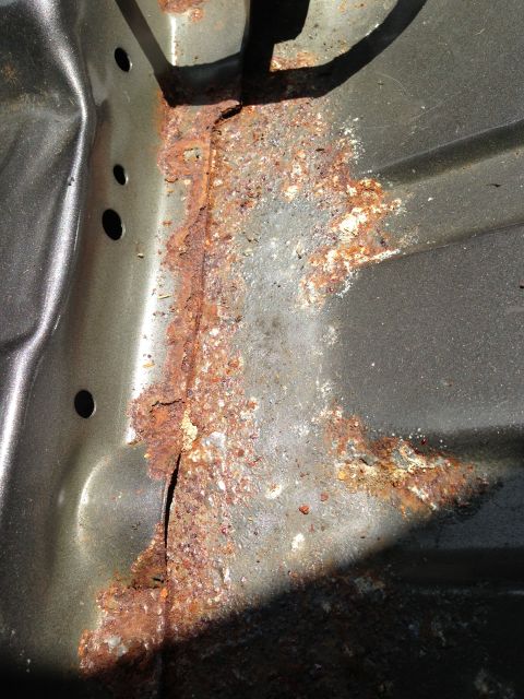 2004 Ford Crown Victoria - This image shows significant rust and corrosion on the underside of a vehicle, likely a floor pan or frame rail. The metal is heavily pitte…
