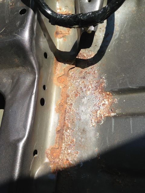 2004 Ford Crown Victoria - This image shows significant rust and corrosion on the metal frame of a vehicle, possibly a 2004 Ford Crown Victoria. A black wire loom is…