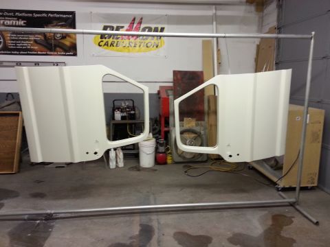1967 Ford F-100 - Two cream-colored vehicle doors hang from a metal rack in a garage. The doors appear to be for a classic pickup truck.