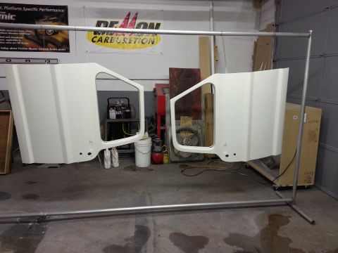 1967 Ford F-100 - Two white vehicle doors are hanging from a metal rack in what appears to be a workshop or garage. An air compressor and other equipment are…