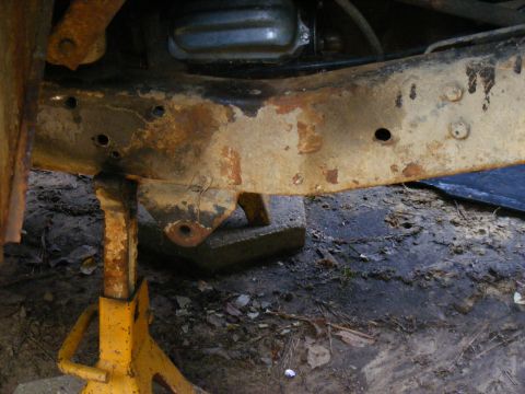 1978 Ford Bronco - The underside of a vehicle shows significant rust and is supported by jack stands.