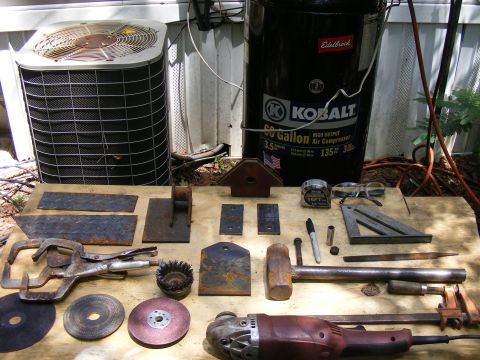 1978 Ford Bronco - Various metalworking tools and supplies are arranged on a wooden surface, including an angle grinder, vise grips, and a large air compresso…
