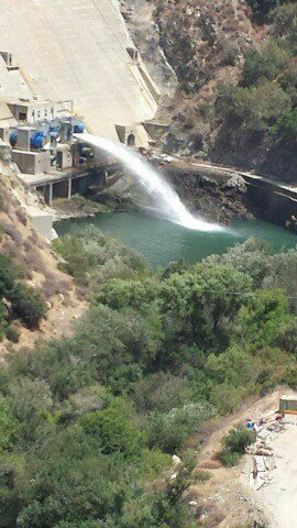 1986 Ford Bronco - Water flows from a dam into a reservoir, surrounded by lush green trees and rocky hills.