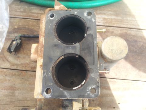 1988 Ford Bronco - A used carburetor with a black gasket and two circular openings sits on a wooden surface.