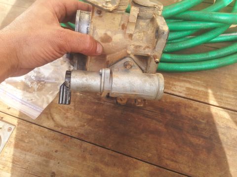 1988 Ford Bronco - A dirty throttle body assembly is held by a hand, with a green hose coiled behind it on a wooden surface.