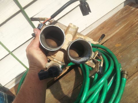 1988 Ford Bronco - Throttle body assembly and garden hose on a wooden surface.